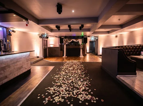 Aisle of ivory and dusty-pink rose petals across the dance floor at Hidden Burnley, leading to a ceremony arch.